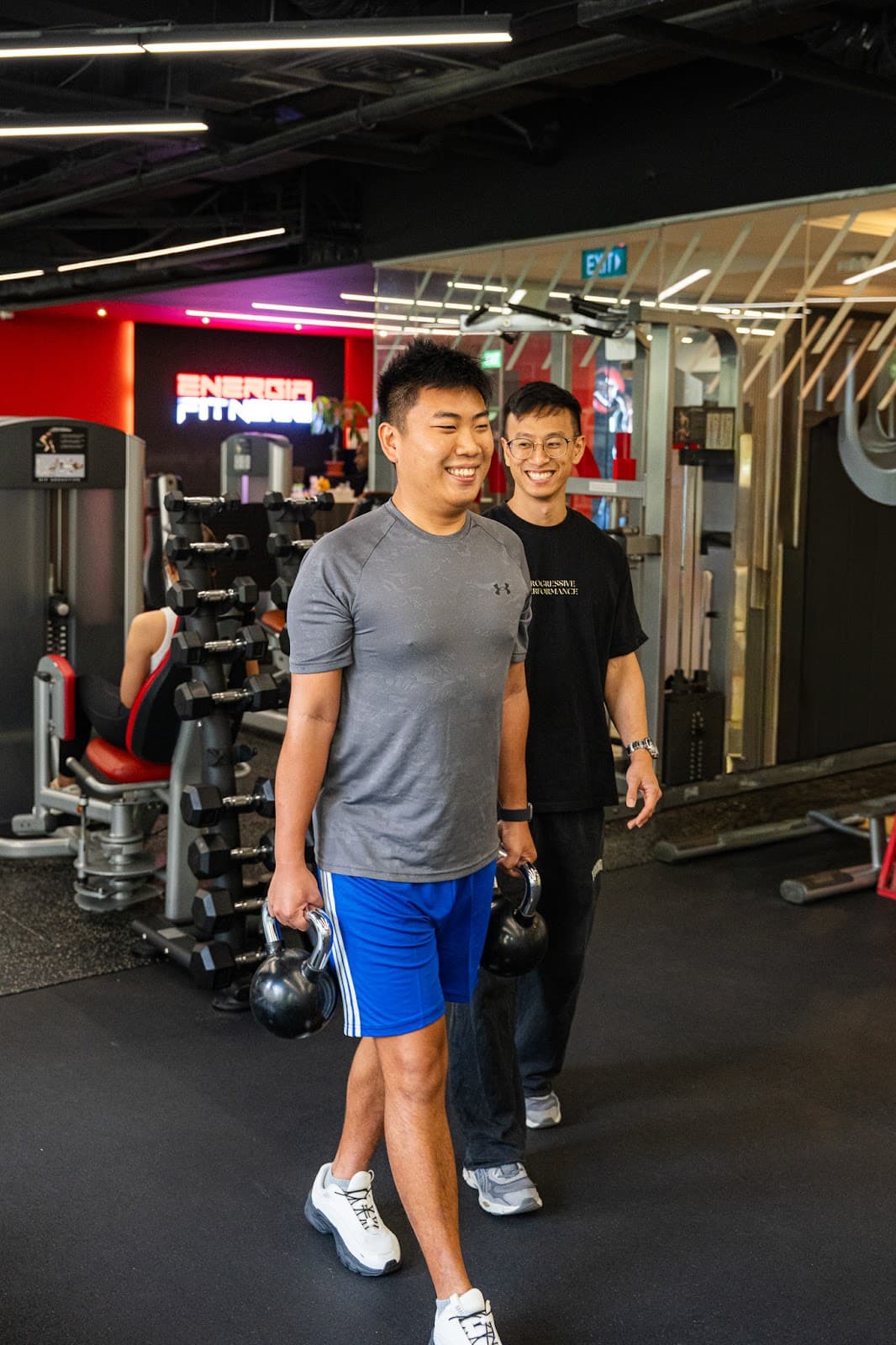 A client carrying kettlebells with a Progressive Performance coach walking behind him.
